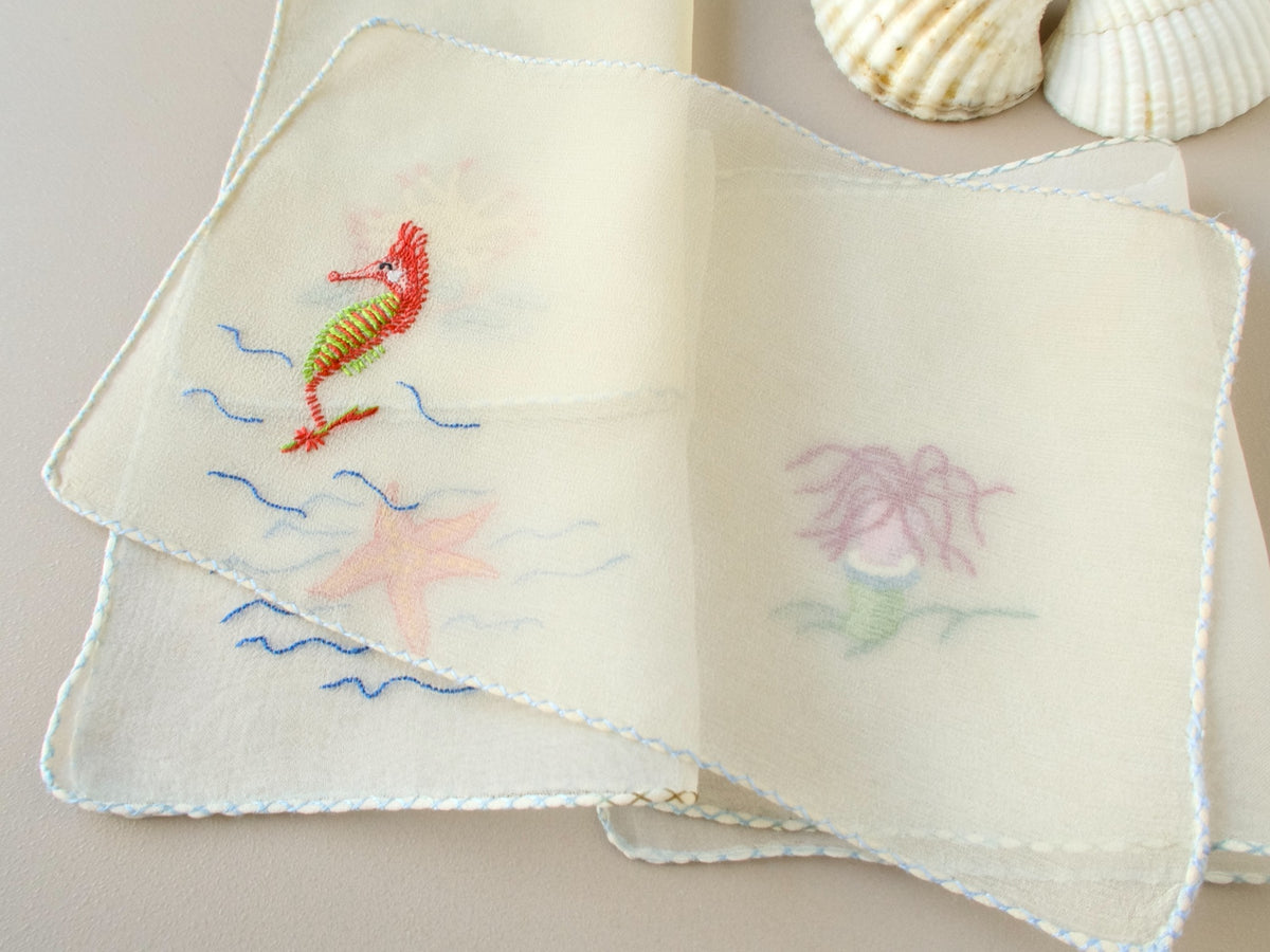 Vintage French silk chiffon cocktail napkins fanned and gathered, showing embroidered sea life motifs and semi-sheer ground.​​​​​​​​​​​​​​​​