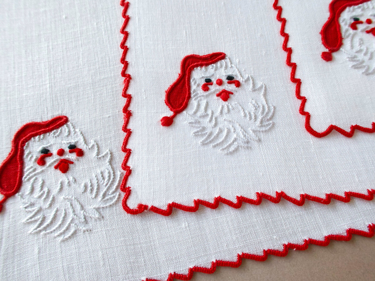 Close-up of vintage Marghab “Papa Noel” cocktail napkin showing raised white beard embroidery and red Santa hat, edge scalloping visible.