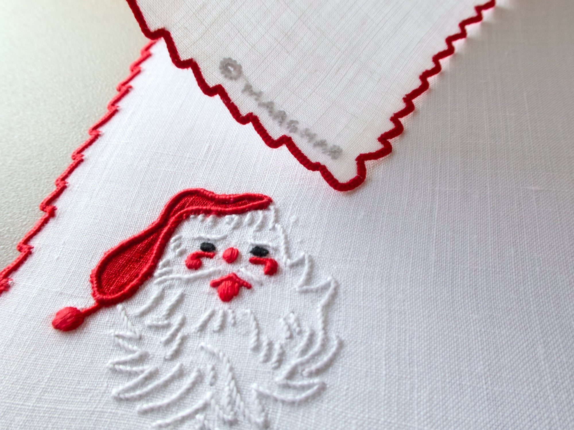 Detail of Marghab “Papa Noel” embroidered Santa motif in red and white thread on fine linen with scalloped border.