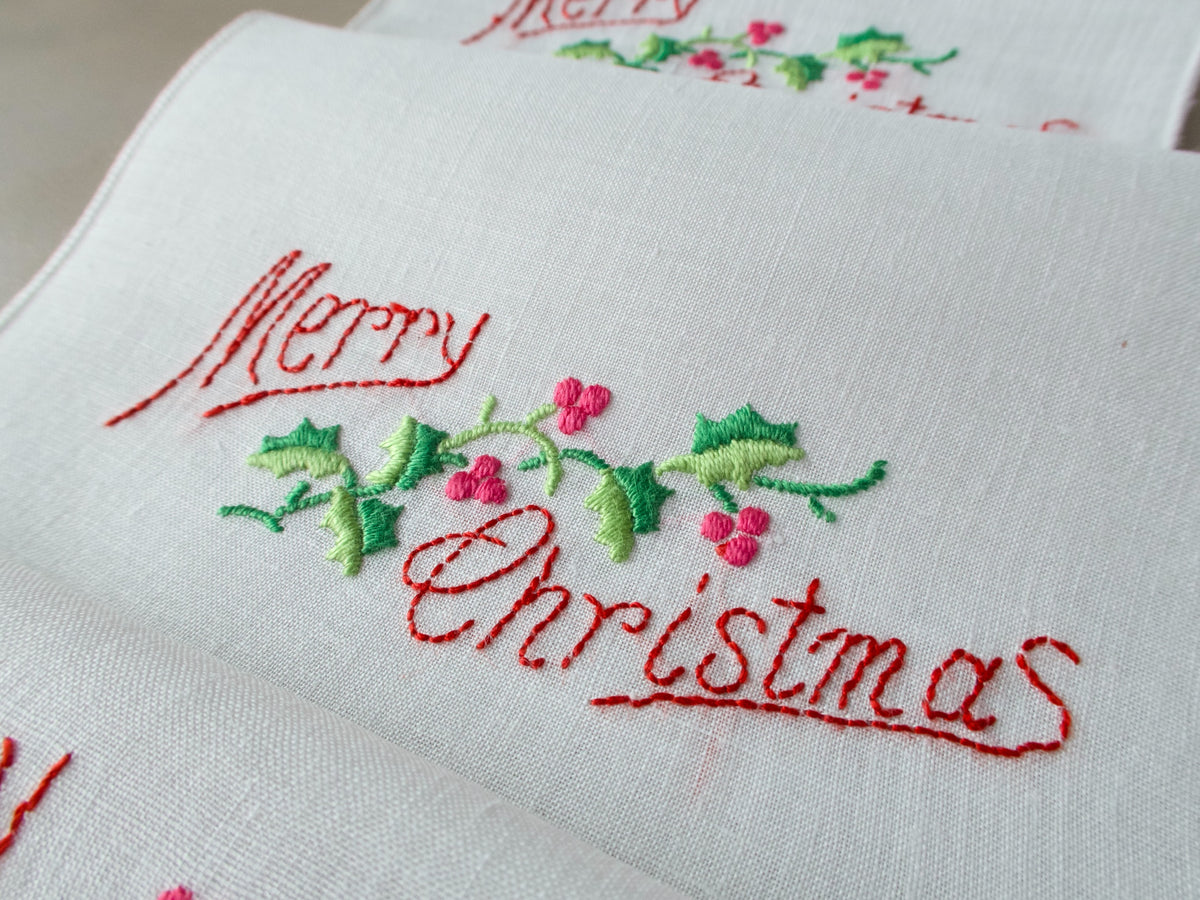  Vintage linen cocktail napkin embroidered with the words "Merry Christmas" and holly on white linen.