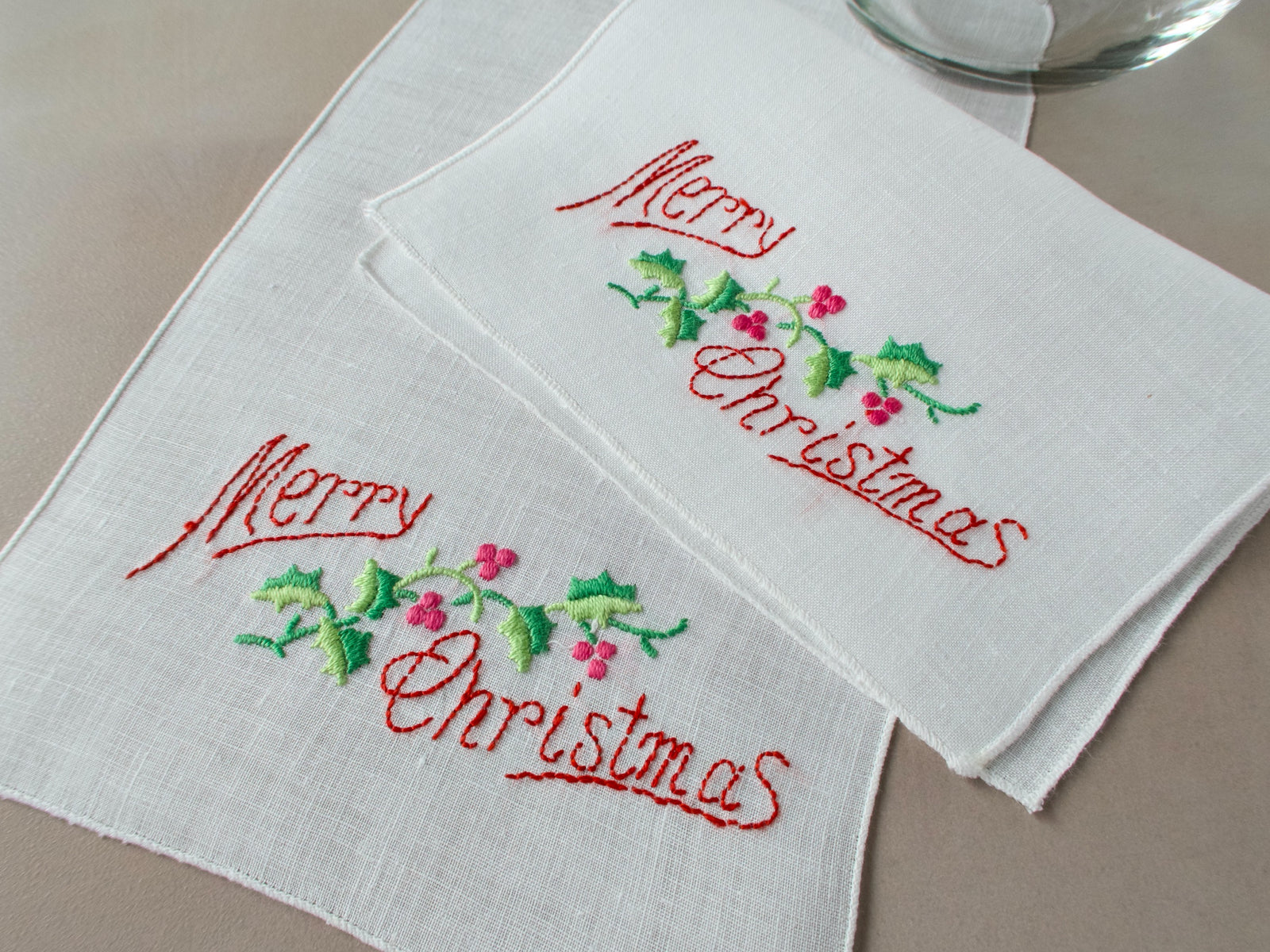 Vintage linen cocktail napkins embroidered with the words "Merry Christmas" and holly on white linen.