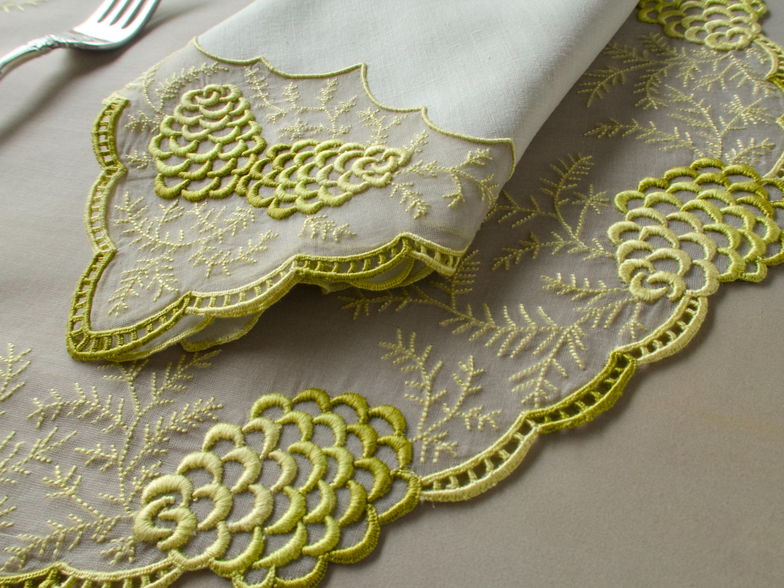 Vintage Marghab napkin with scalloped hem draped over a placemat embroidered with raised pine cones