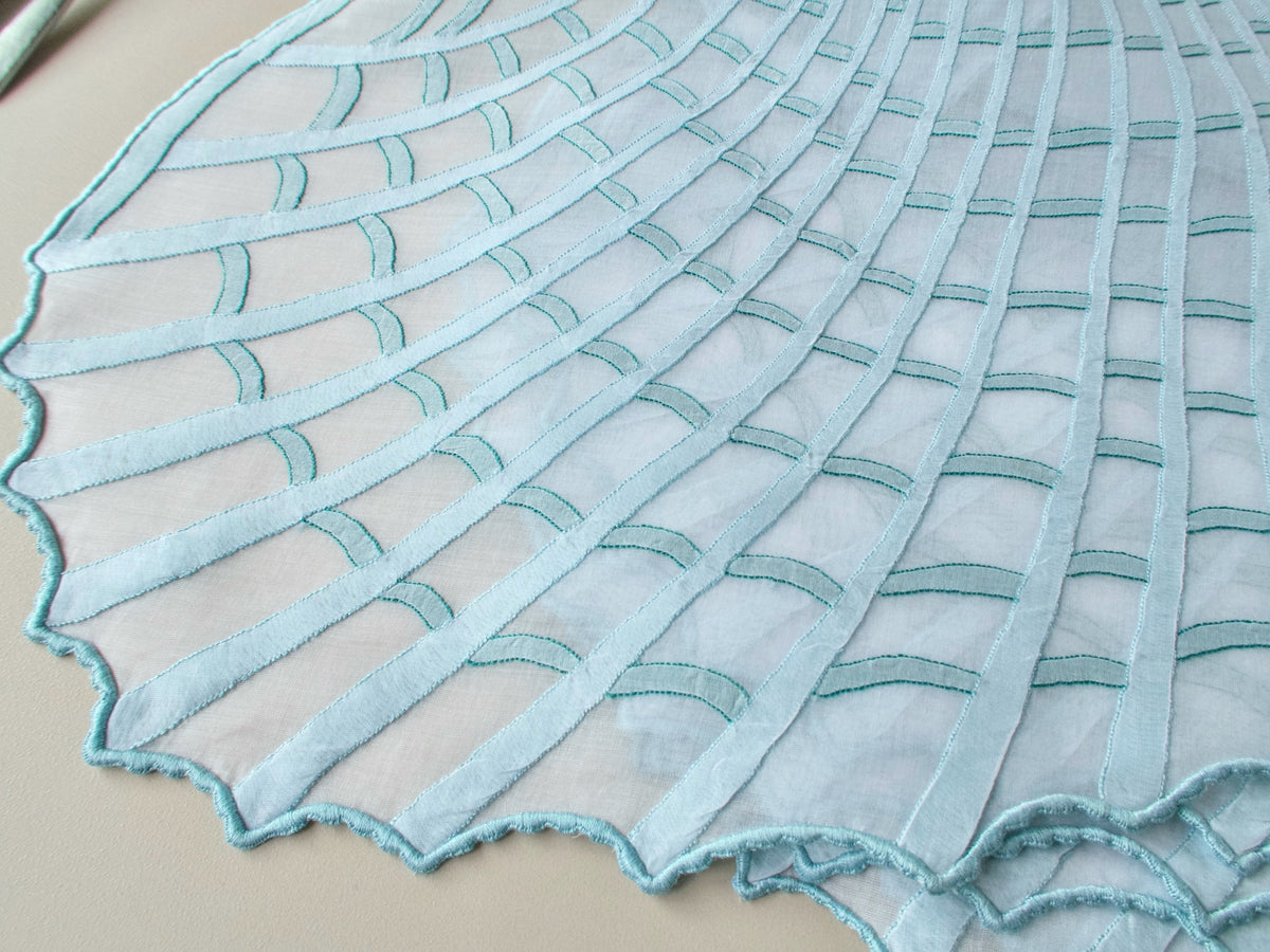 Full view of shell-shaped Léron organdy placemat showing sculptural form and shadow work embroidery, beige background
