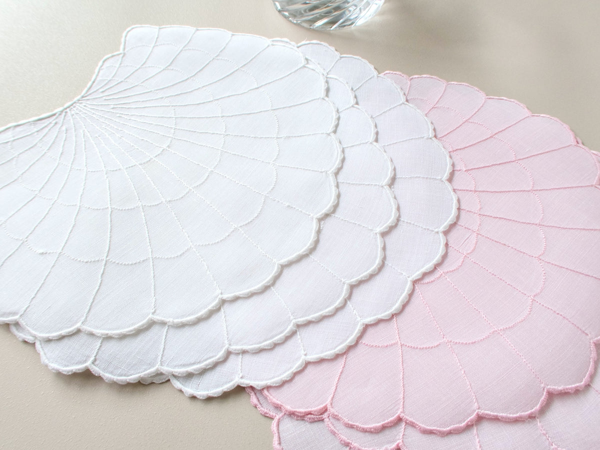 Pink and white scallop shell-shaped Madeira cocktail napkins, cut linen, with radiating embroidered lines and scalloped edges.