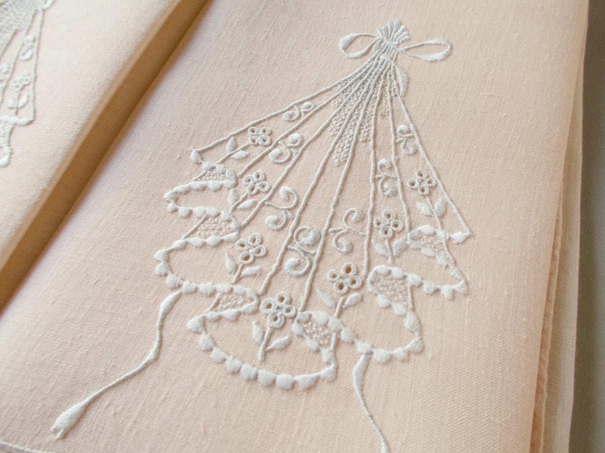 Close-up of pale peach linen guest towel with white embroidered cascading motif and bow-shaped top detail.