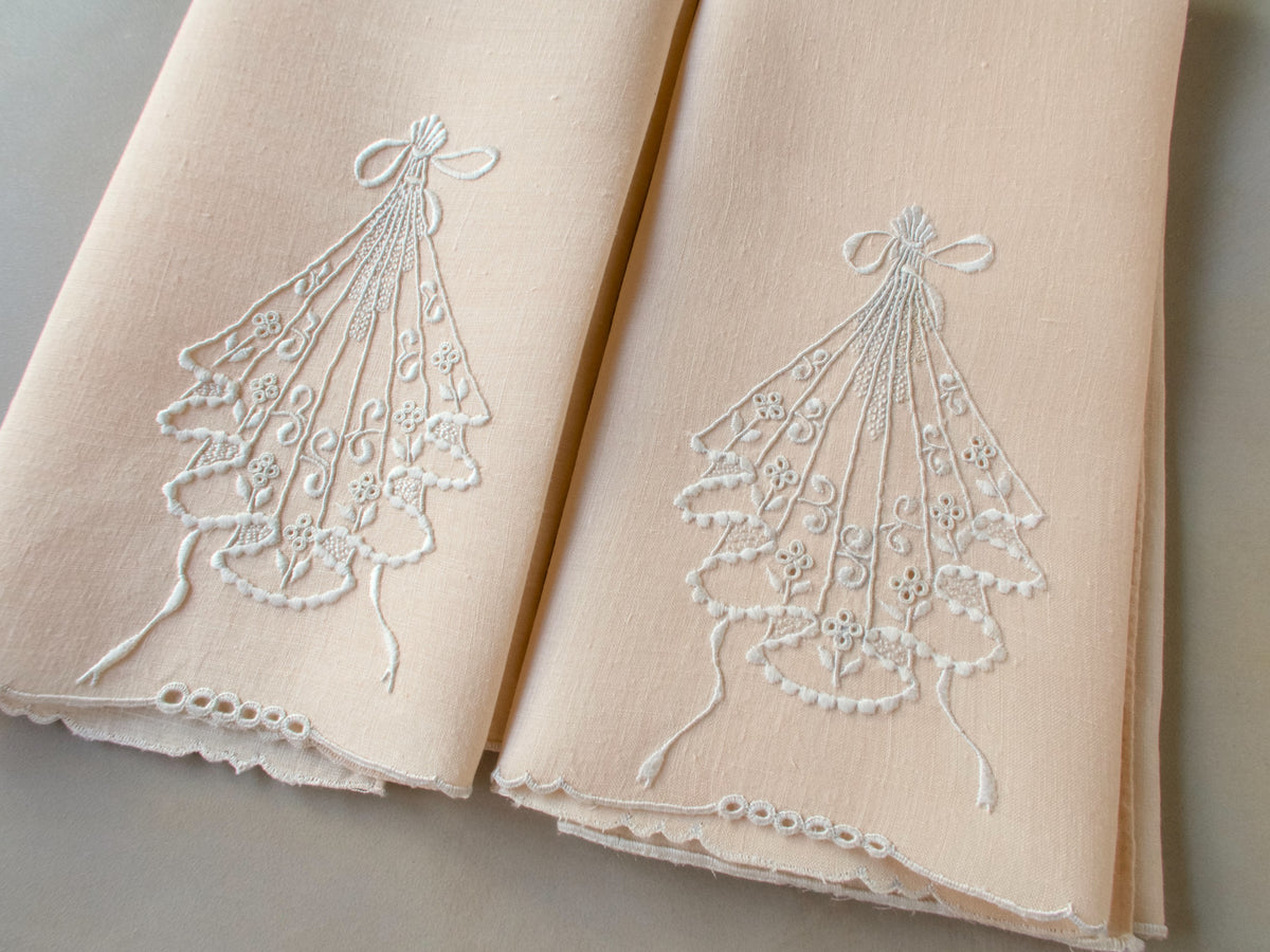 Pair of pale peach linen guest towels with white embroidered cascading motif and bow-shaped top detail.