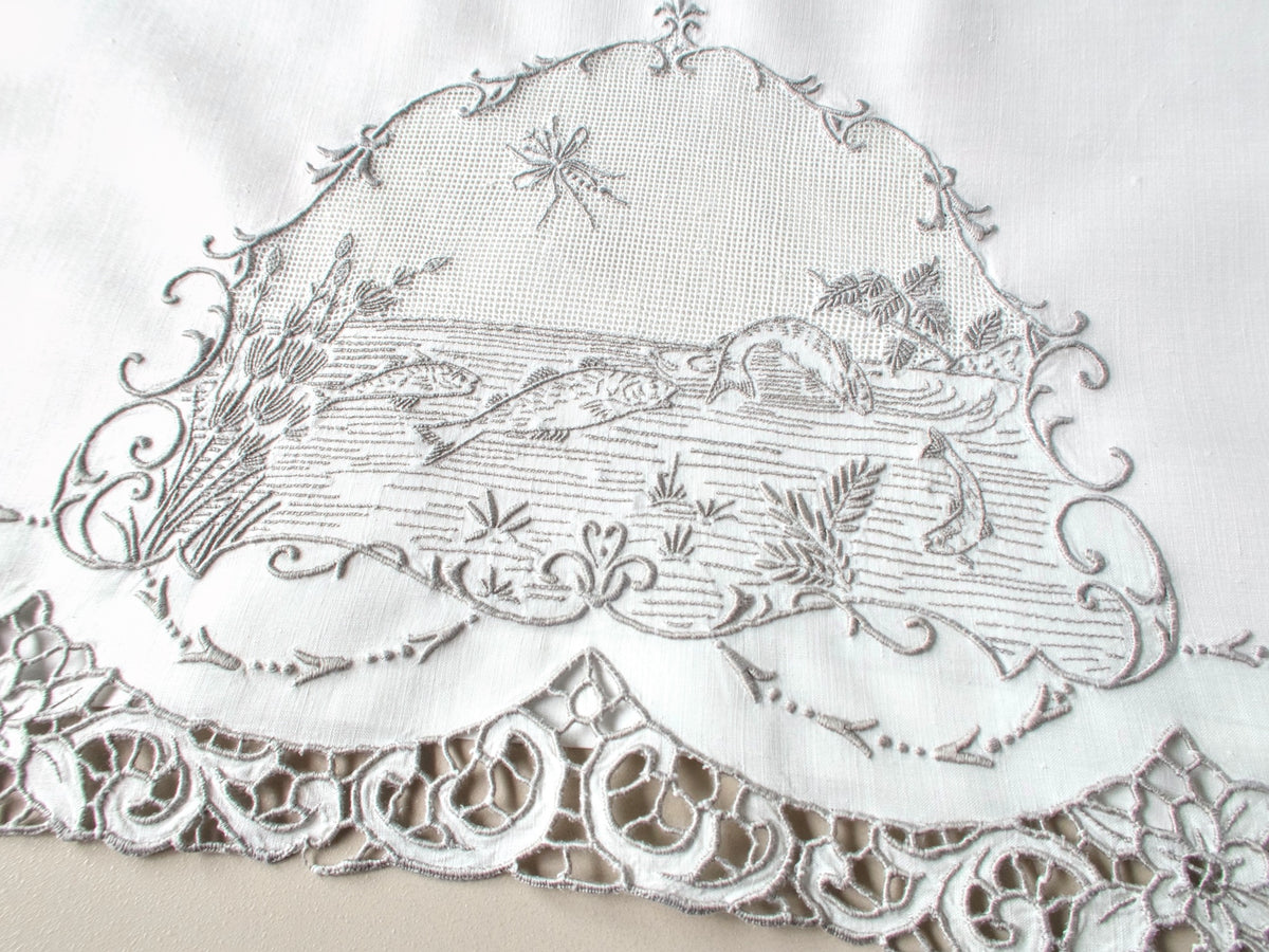 Antique Italian hand embroidered guest towel, fish swimming among reeds and water plants beneath open mesh sky with dragonfly, scrolling floral border.