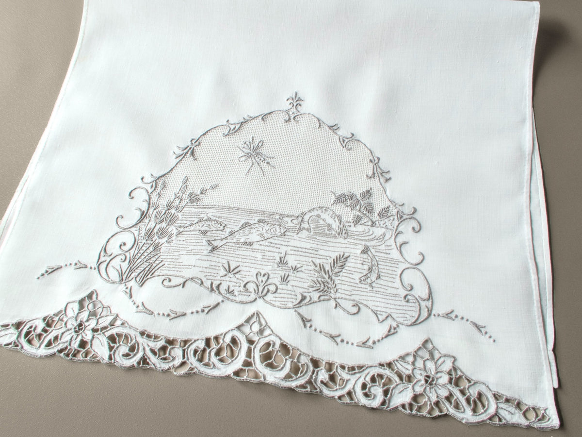 Antique Italian hand embroidered guest towel, fish swimming among reeds and water plants beneath open mesh sky with dragonfly, scrolling floral border.