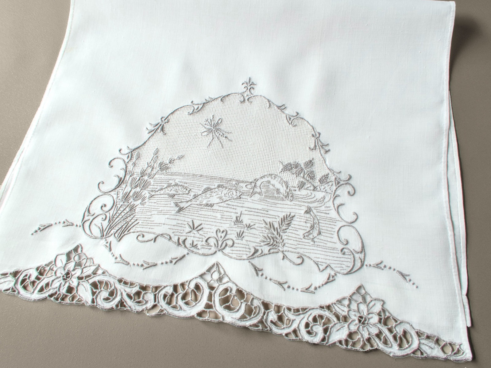 Antique Italian hand embroidered guest towel, fish swimming among reeds and water plants beneath open mesh sky with dragonfly, scrolling floral border.