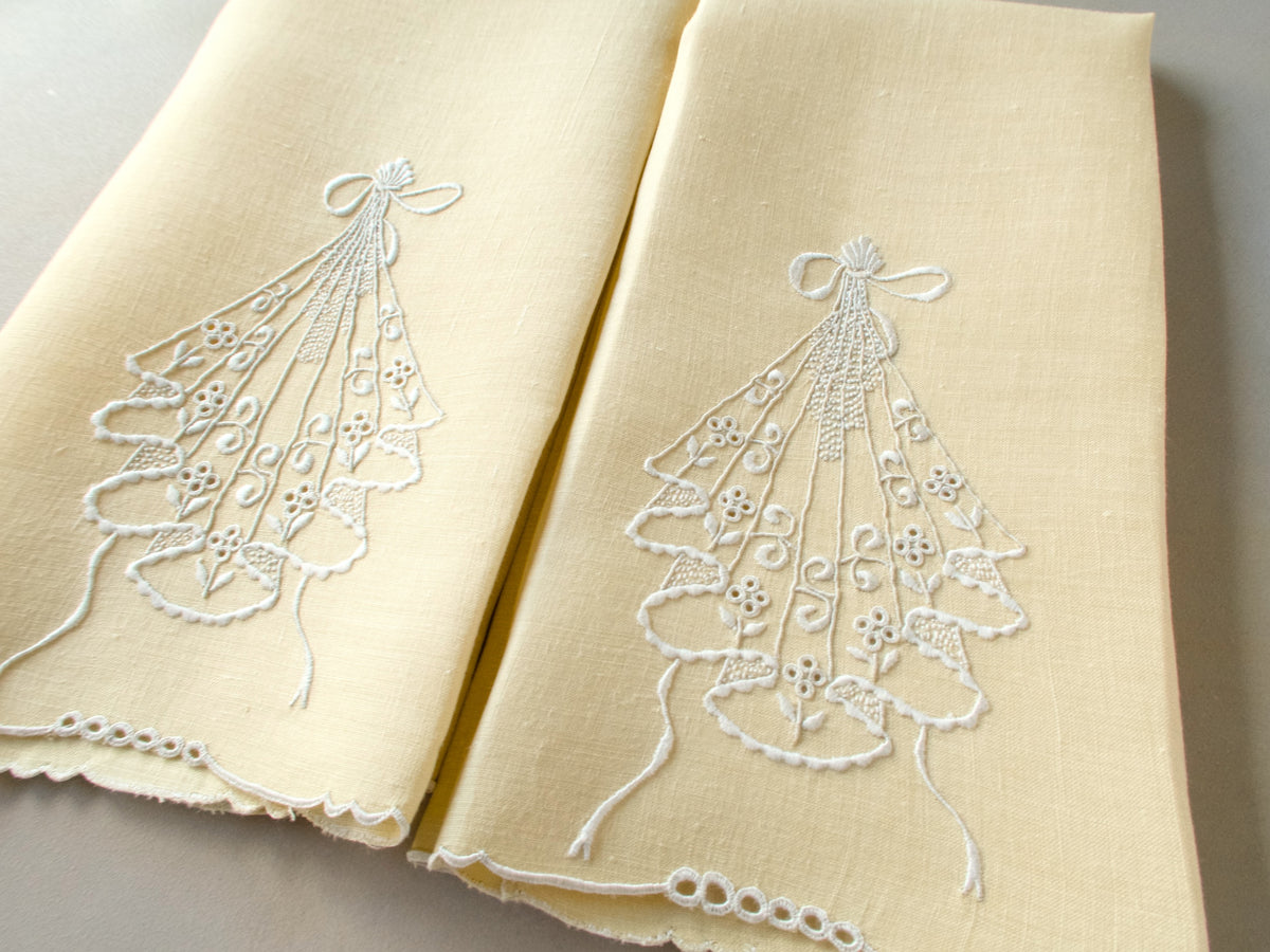 Pair of pale yellow linen guest towels with white embroidered cascading motif and bow-shaped top detail.