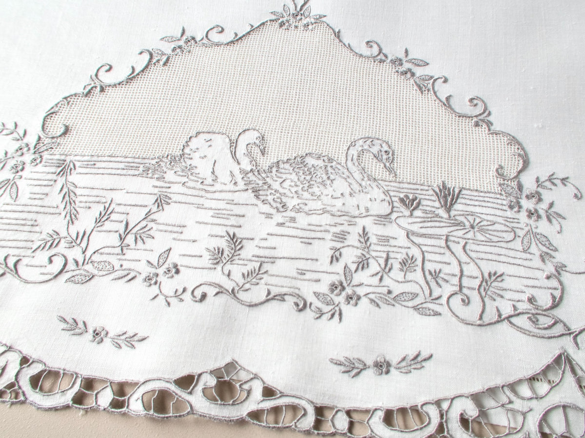 Antique Italian hand embroidered guest towel, two swans swimming among lily pads and flowering vines beneath open mesh sky, scrolling floral border.