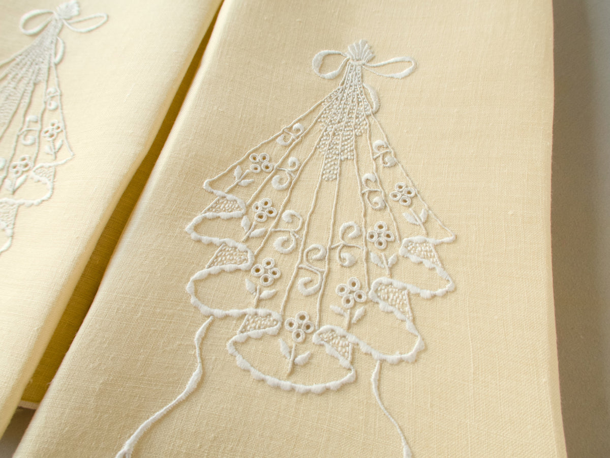 Close-up of pale yellow linen guest towel with white embroidered cascading motif and bow-shaped top detail.
