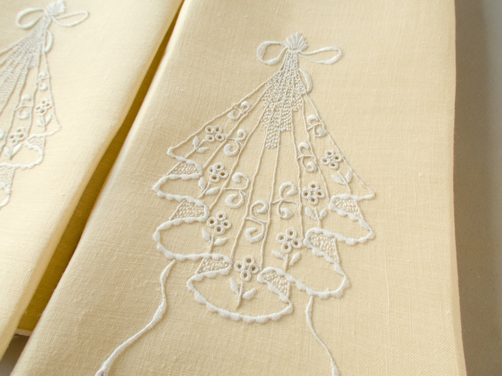 Close-up of pale yellow linen guest towel with white embroidered cascading motif and bow-shaped top detail.