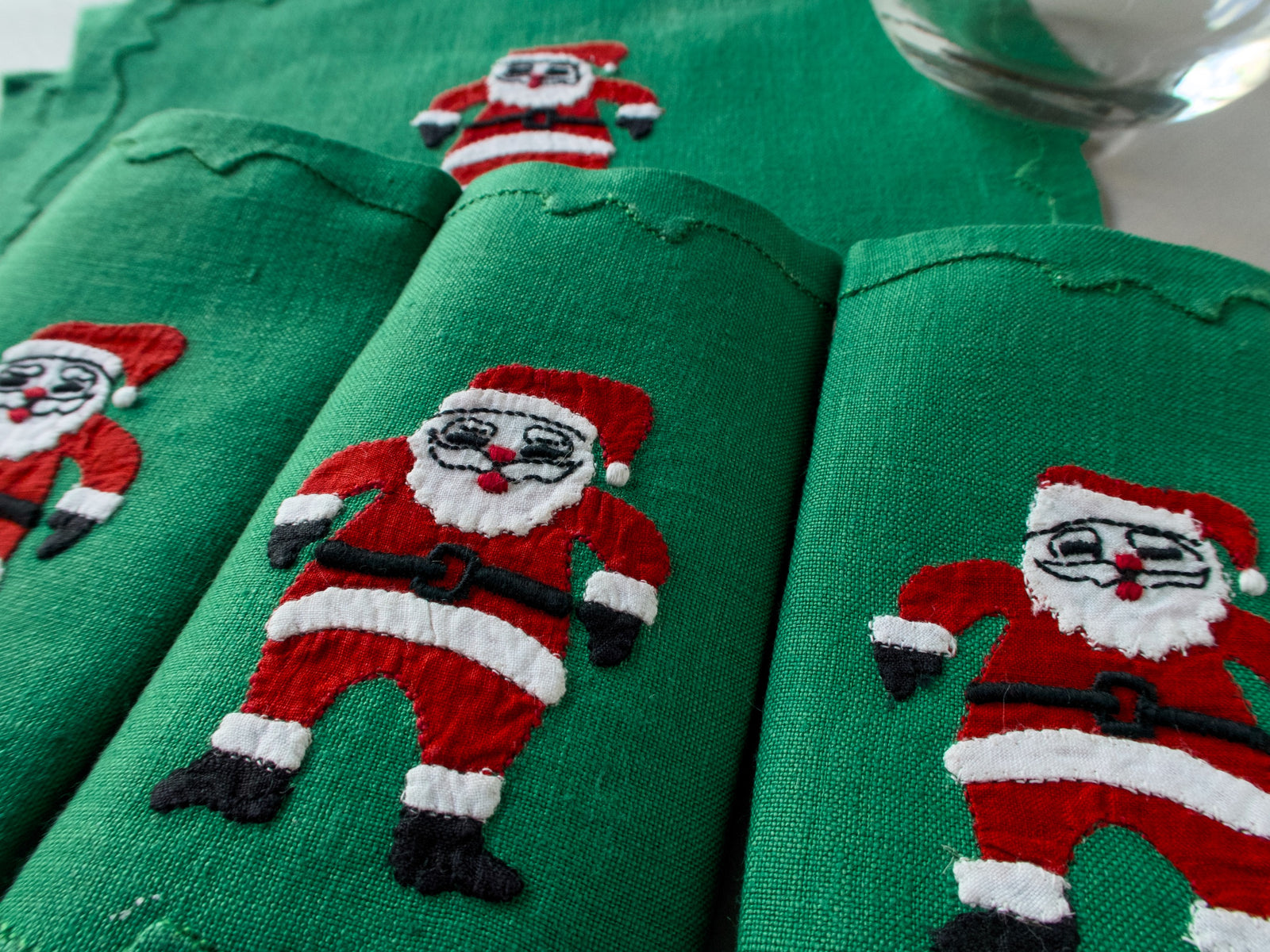 Green linen cocktail napkins with a hand-embroidered Santa in a red suit, close-up, handmade in Madeira