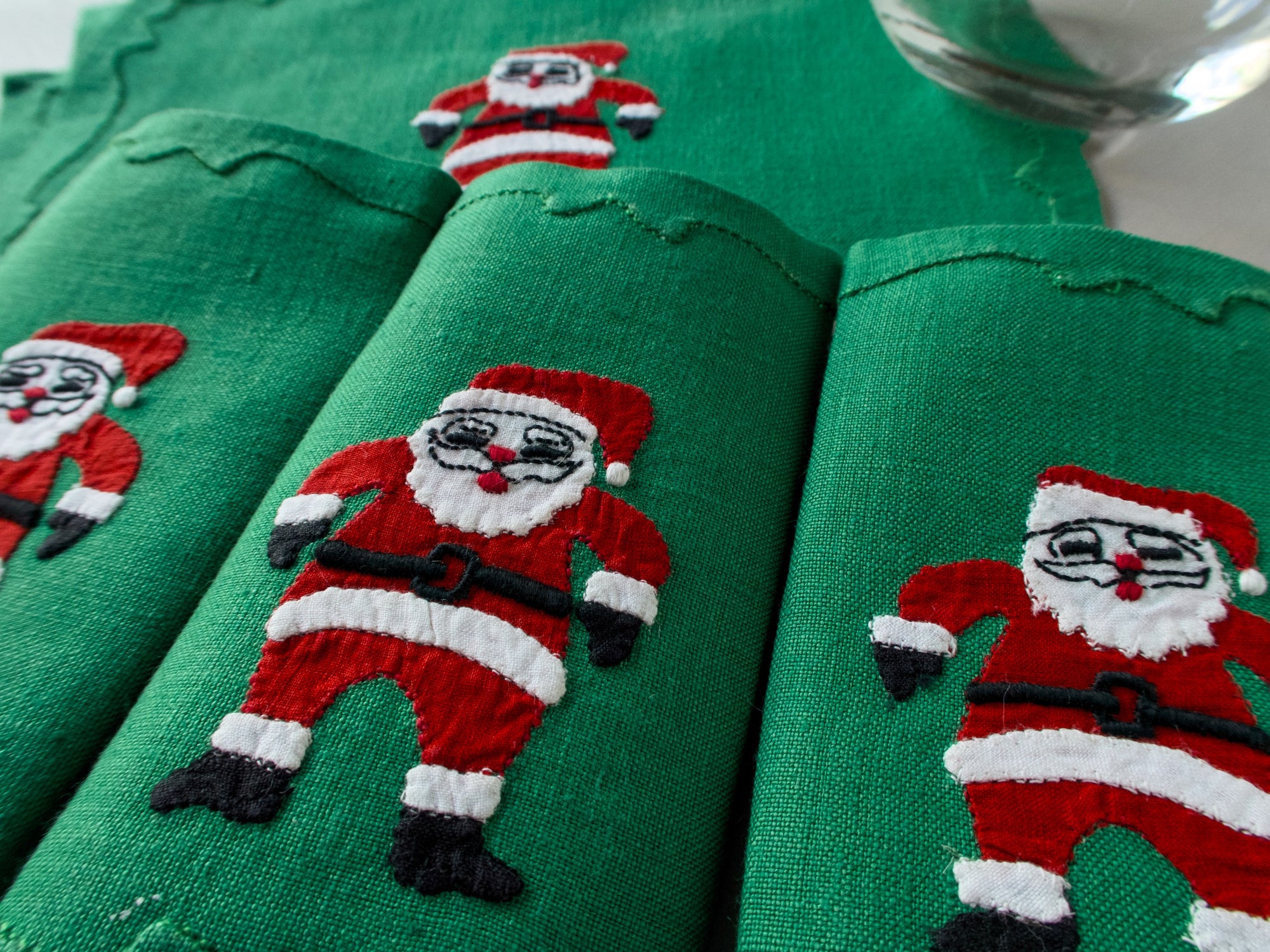 Green linen cocktail napkins with a hand-embroidered Santa in a red suit, close-up, handmade in Madeira
