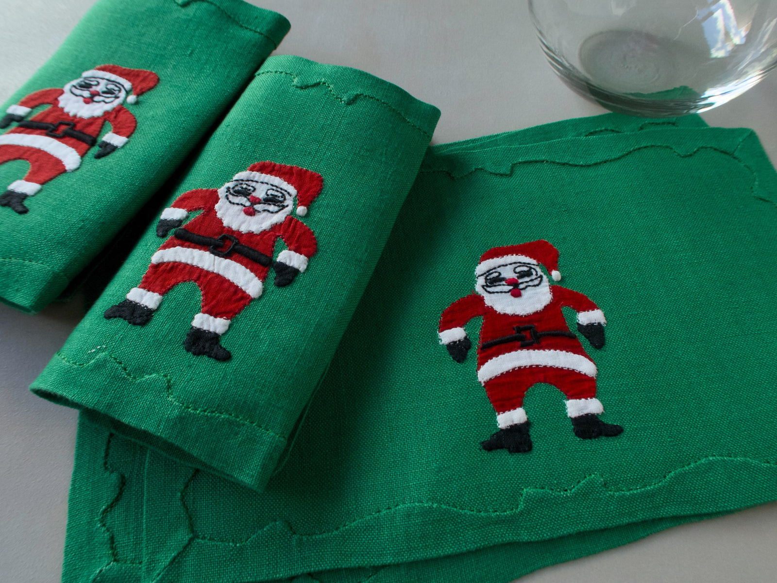 Green linen cocktail napkins with  hand-embroidered Santas in red suits,  handmade in Madeira