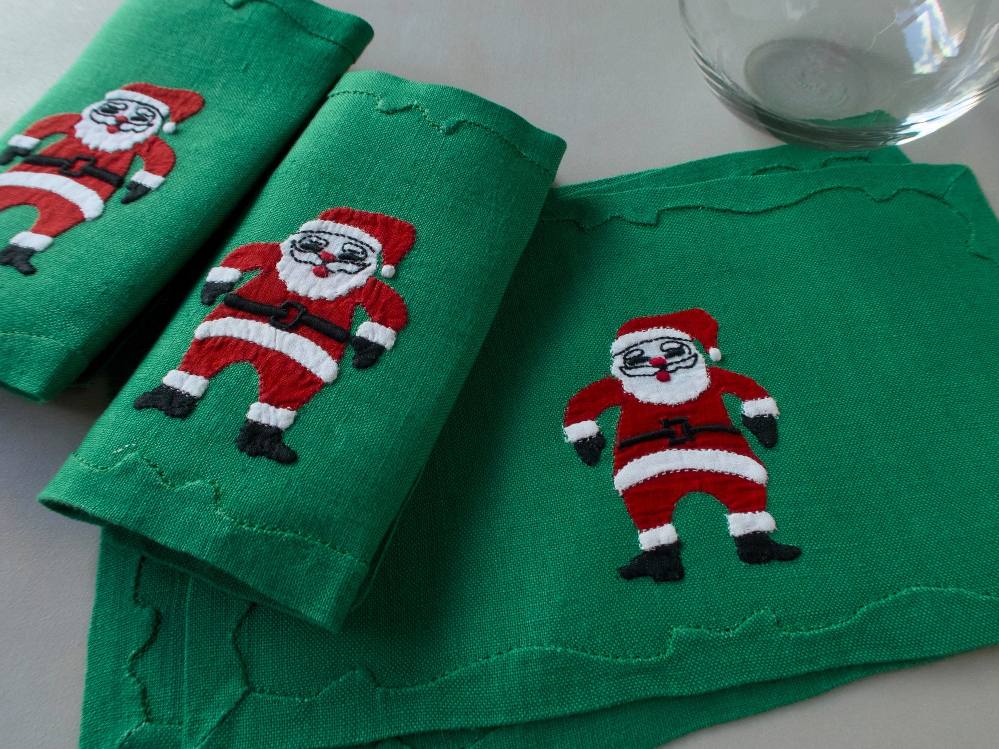 Green linen cocktail napkins with  hand-embroidered Santas in red suits,  handmade in Madeira