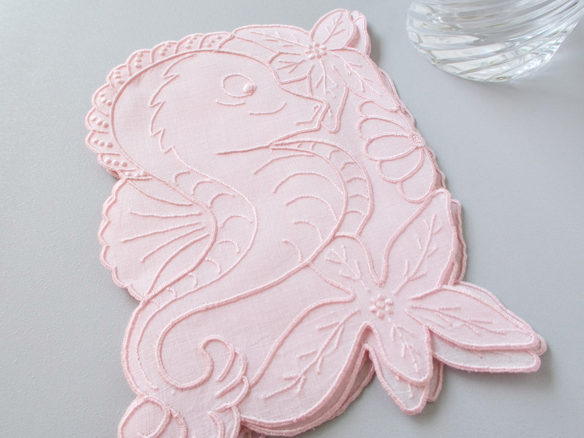 Stacked pink vintage Madeira linen cocktail napkins each in the shape of a seahorse surrounded by hand embroidered tropical flowers and scalloped edges