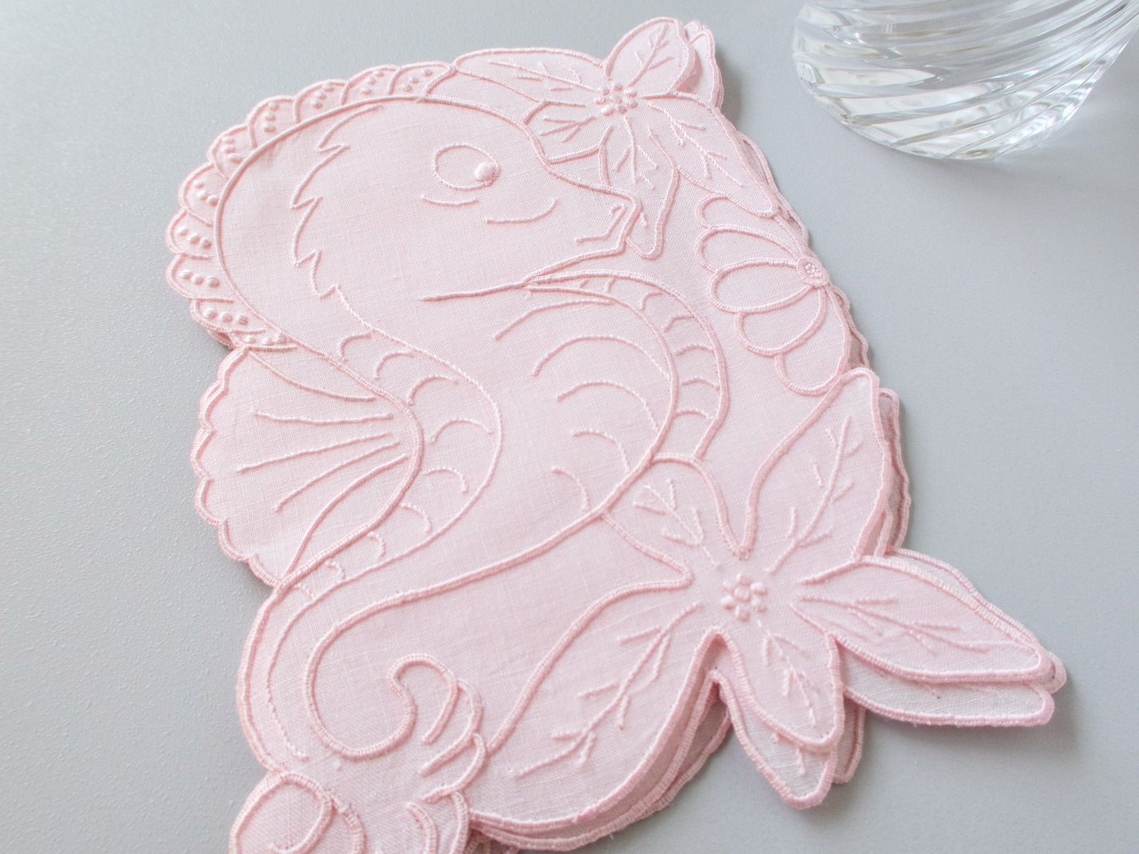 Stacked pink vintage Madeira linen cocktail napkins each in the shape of a seahorse surrounded by hand embroidered tropical flowers and scalloped edges