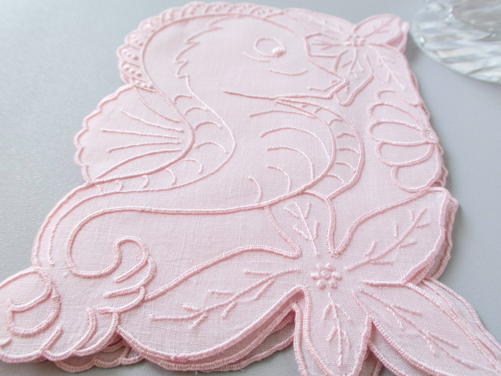 Close-up of vintage Madeira seahorse cocktail napkin showing fine pink linen and detailed hand embroidery​​​​​​​​​​​​​​​​