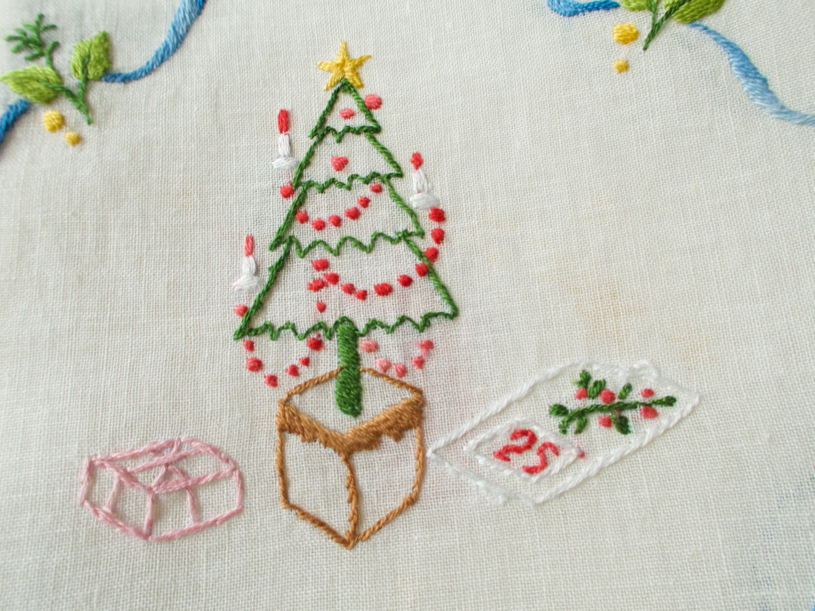 Close-up of embroidered candle-lit tree motif on linen background, showing star and ribbon details.