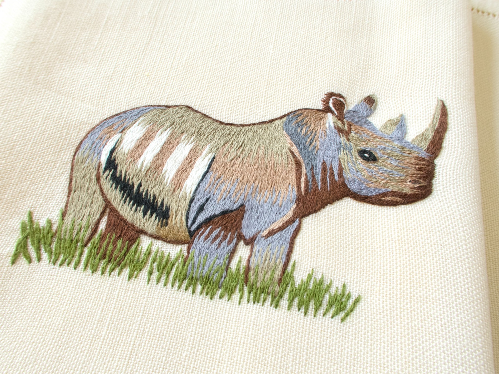 Close-up of vintage hand embroidered placemat showing detailed rhino in grass on  linen