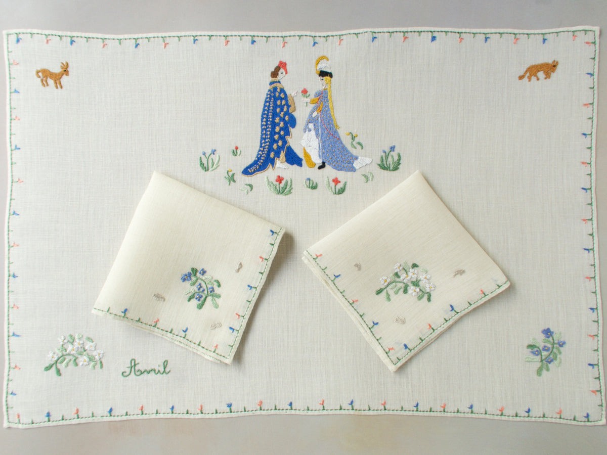 April breakfast set with centerpiece and two napkins arranged together, showing the embroidered couple and scattered florals.