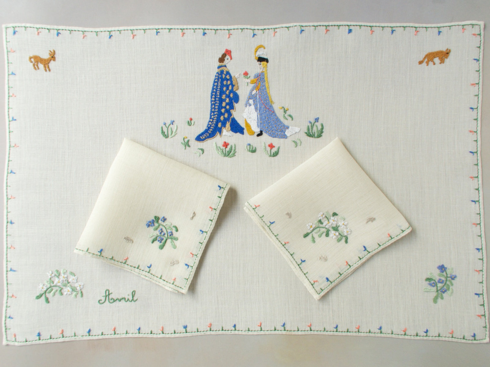 April breakfast set with centerpiece and two napkins arranged together, showing the embroidered couple and scattered florals.