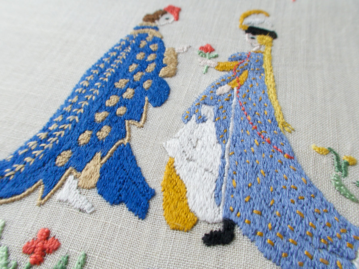 Angled view of the April breakfast set with medieval figures, floral embroidery and neatly folded napkins on light linen.