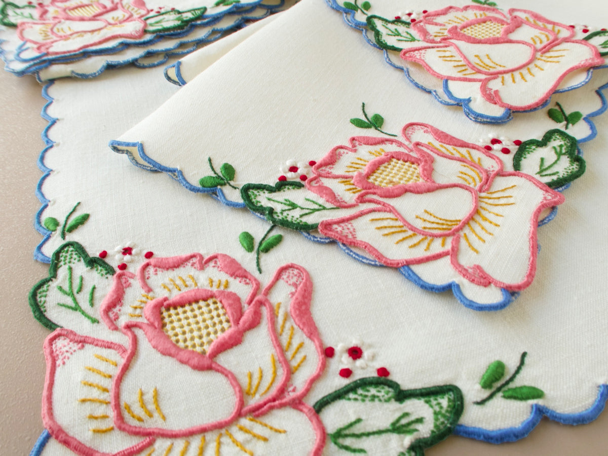 Close-up detail of vintage Madeira tea napkin showing pink rose embroidery with drawnwork center and red berry detail on cream linen​​​​​​​​​​​​​​​​