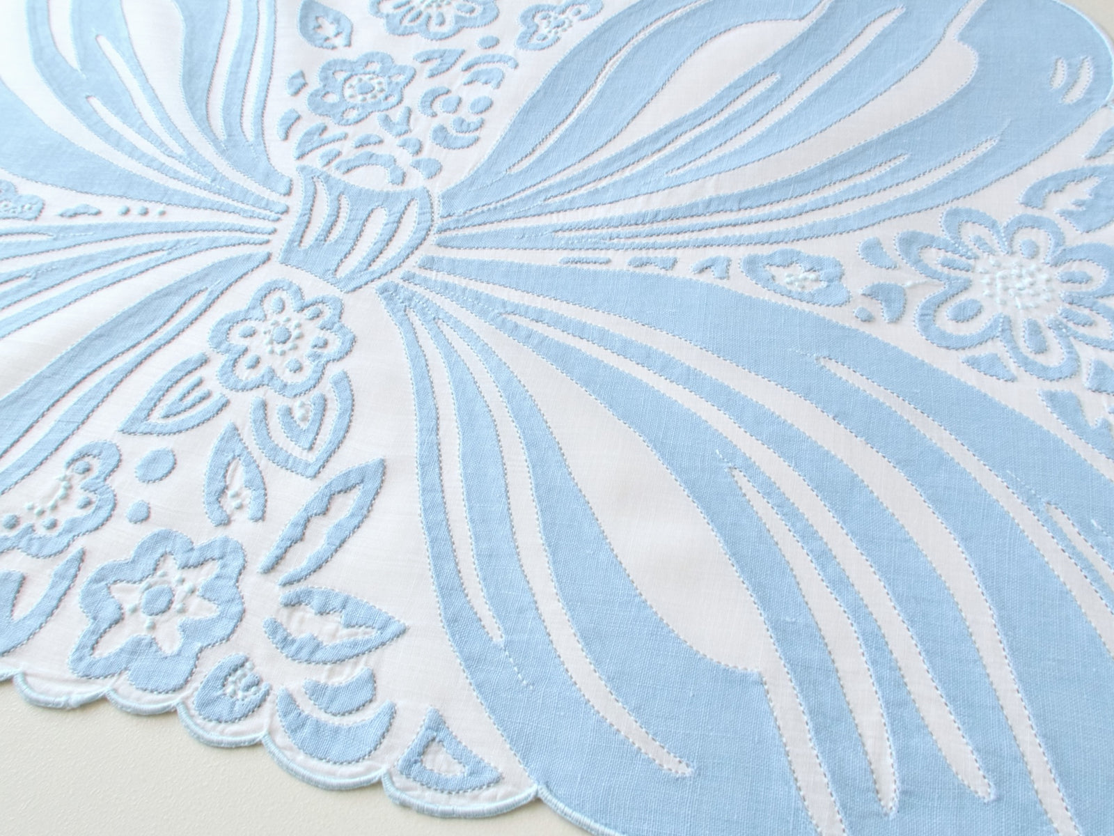 Close up detail of blue bow in embroidery and applique, vintage Madeira hand embroidered placemat set.