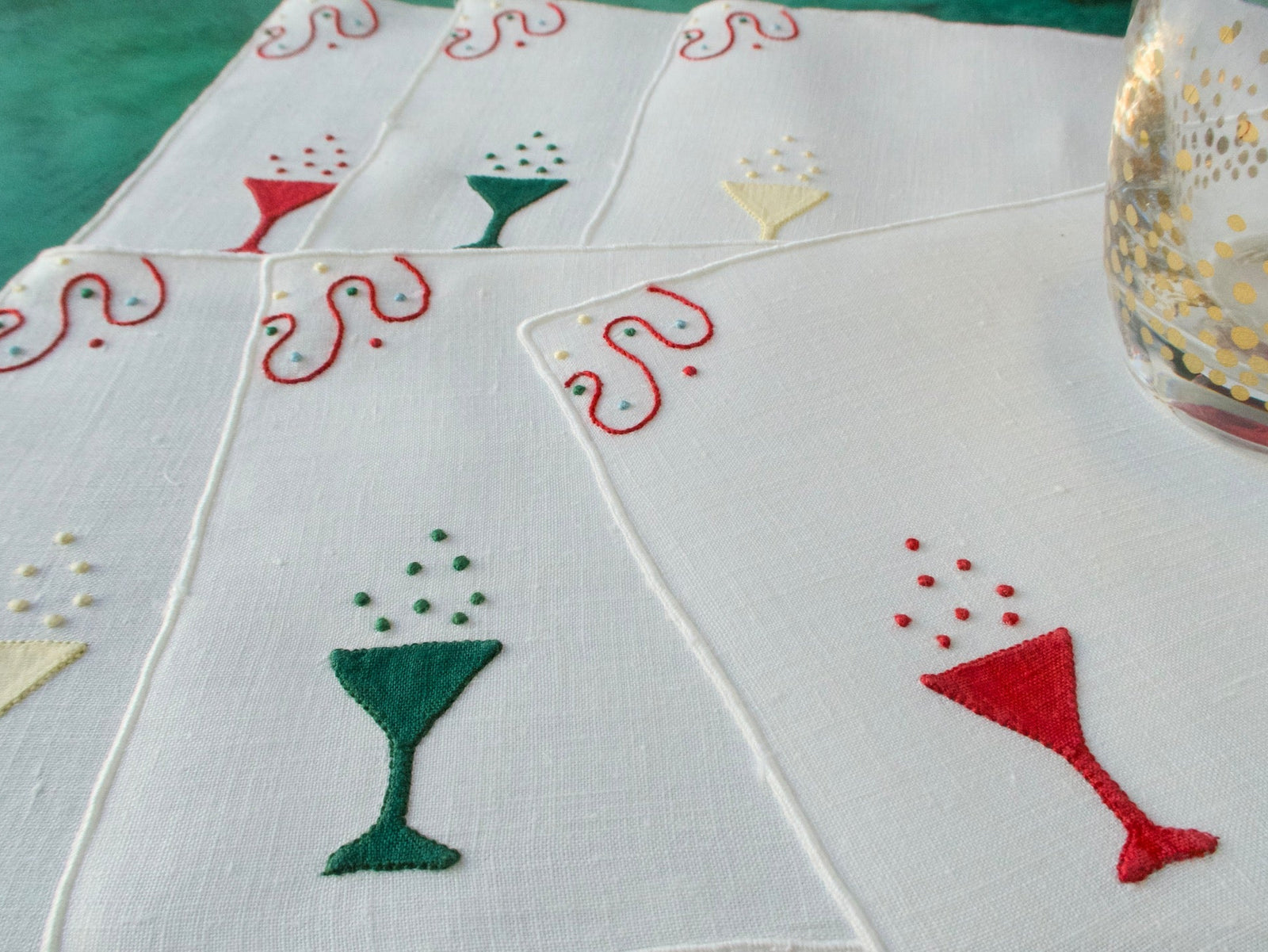 White linen cocktail napkins embroidered with champagne glasses in red, green and yellow, arranged in a group.