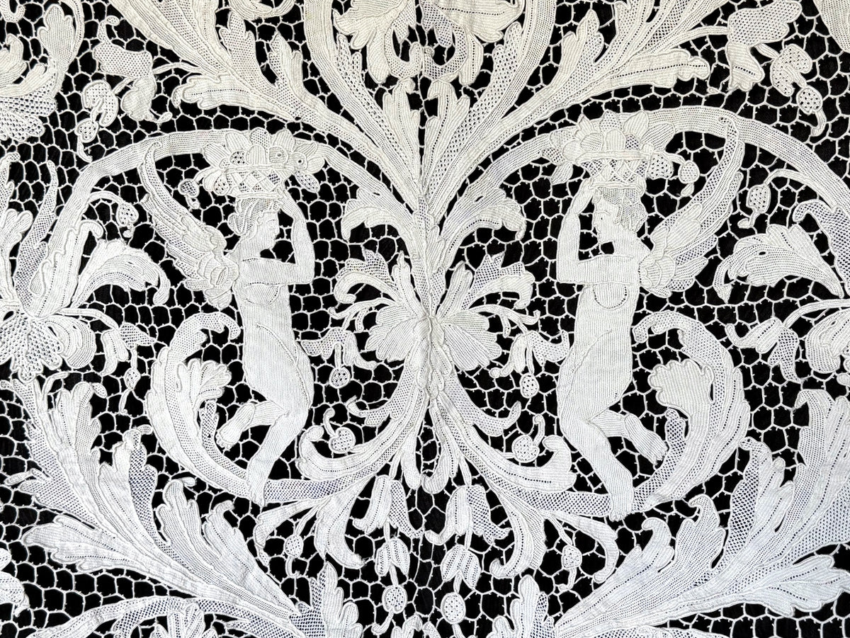 Two winged figures bearing baskets amid flowers and scrolling leaves in the lace.