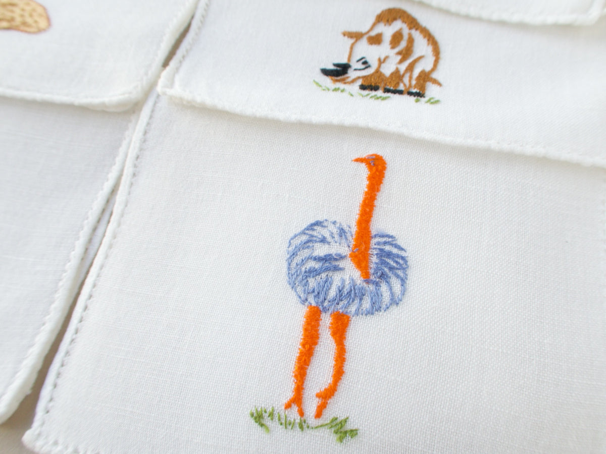 Close-up of vintage Italian cocktail napkin showing embroidered ostrich with orange legs and blue plumage