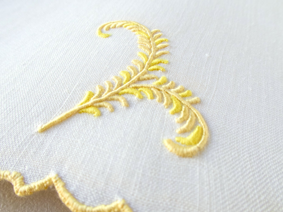 Vintage Madeira linen cocktail napkin detail with yellow plume embroidery and visible linen weave.