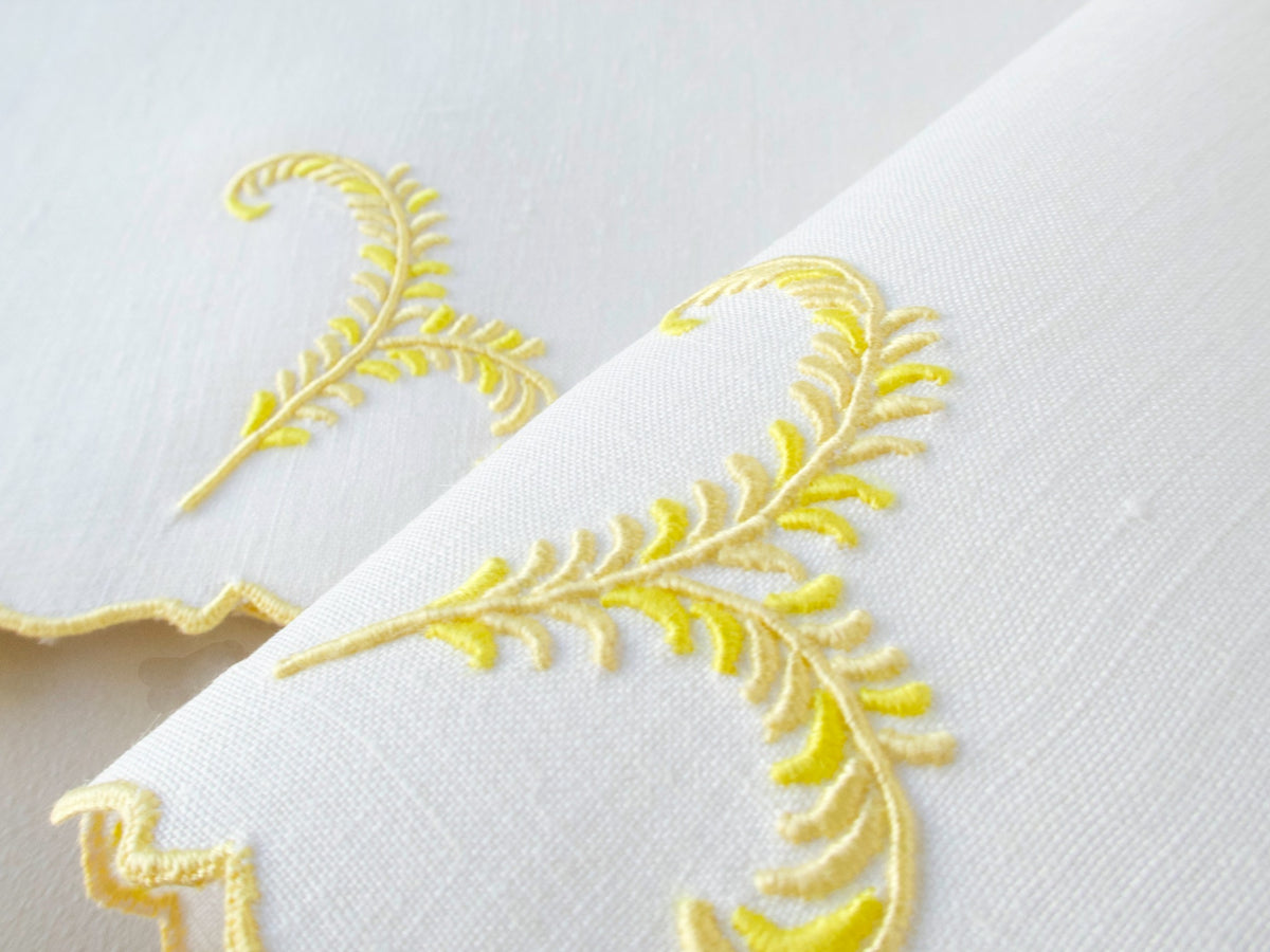Close view of vintage Madeira linen cocktail napkins with yellow plume embroidery and scalloped edge detail