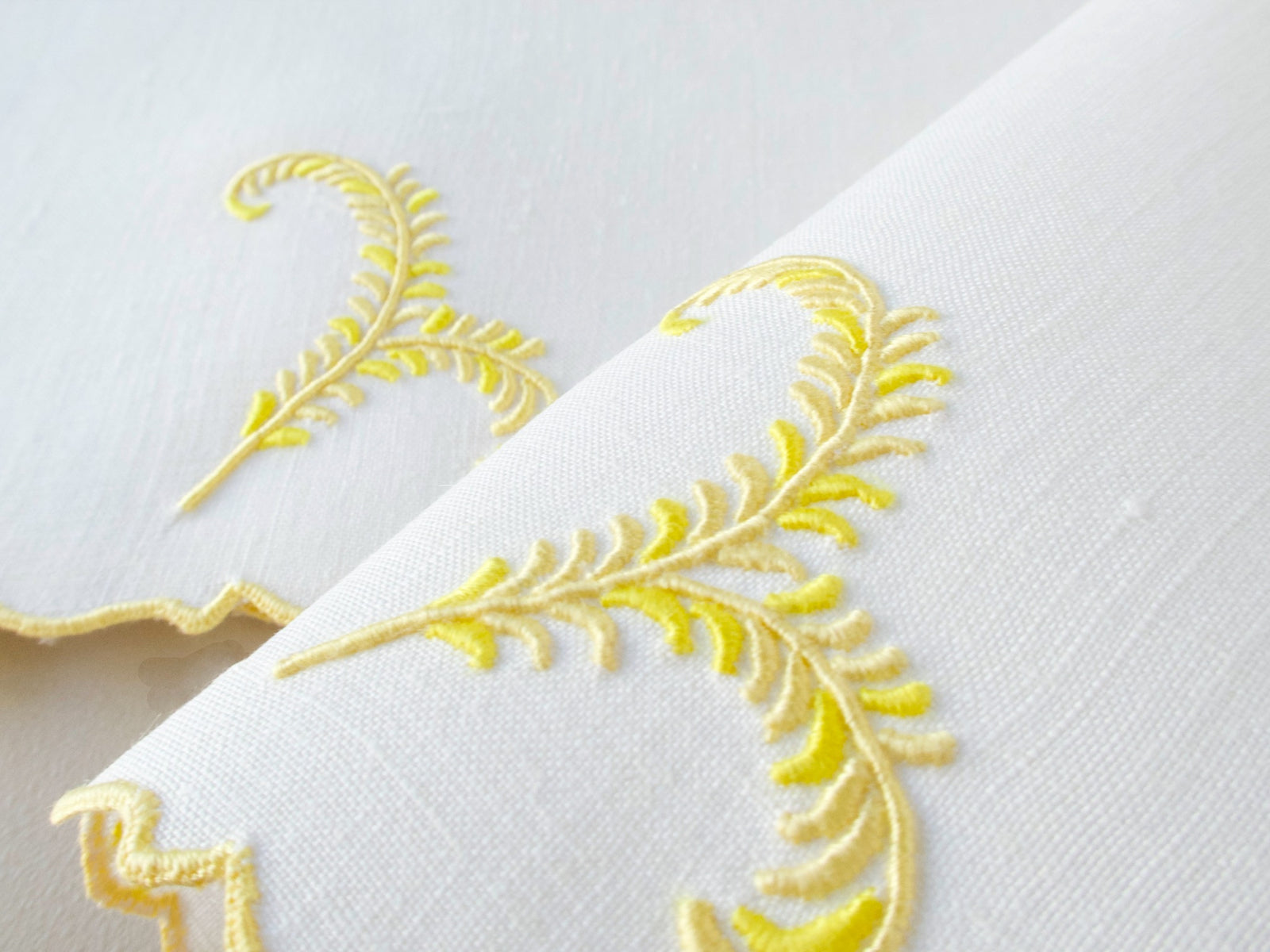 Close view of vintage Madeira linen cocktail napkins with yellow plume embroidery and scalloped edge detail