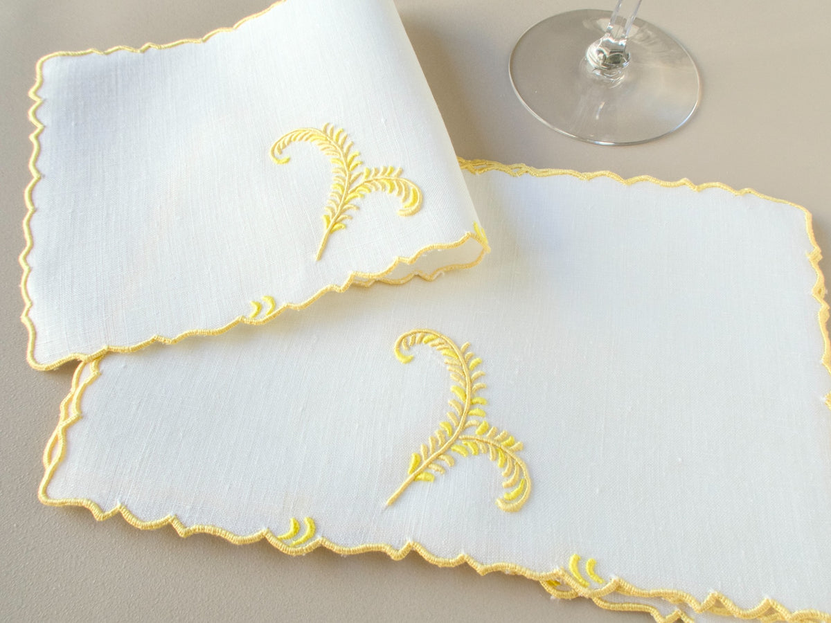 Vintage Madeira linen cocktail napkins with yellow plume embroidery and scalloped edges, shown with glass