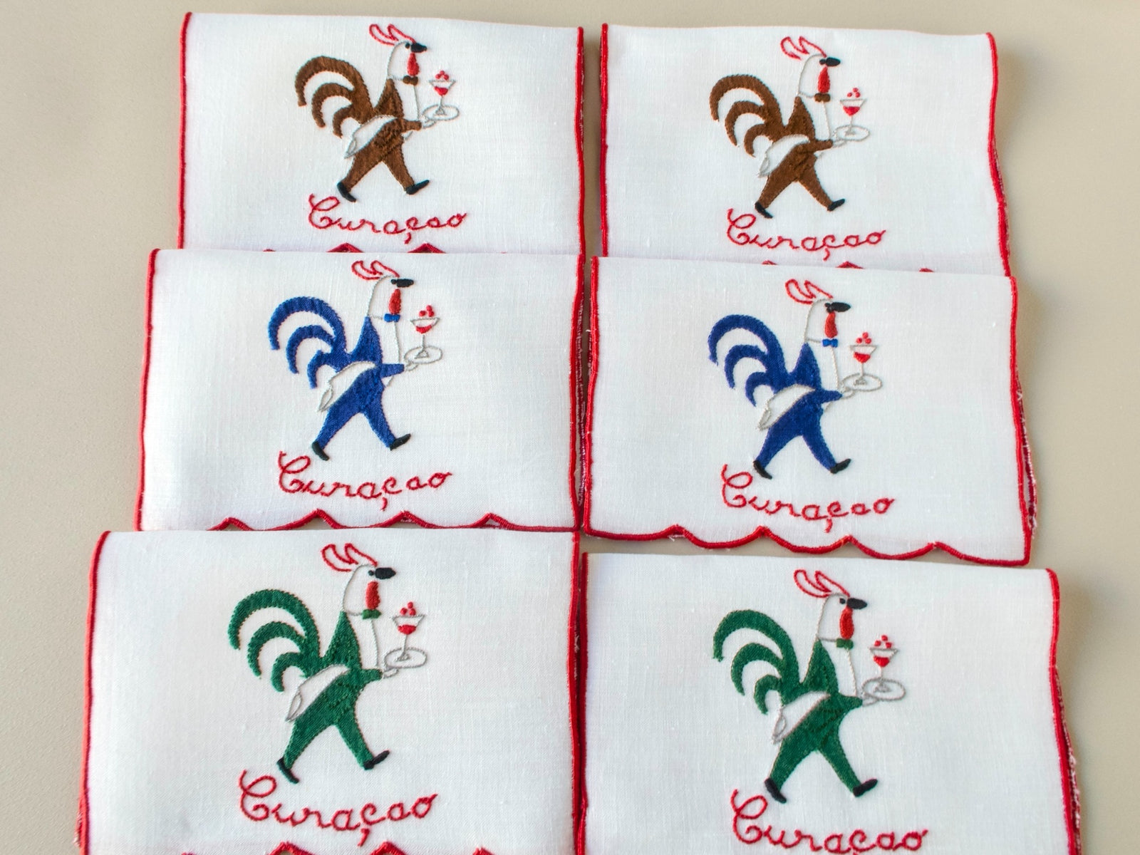 Folded set of vintage Madeira hand embroidered rooster cocktail napkins, white linen with red trim.