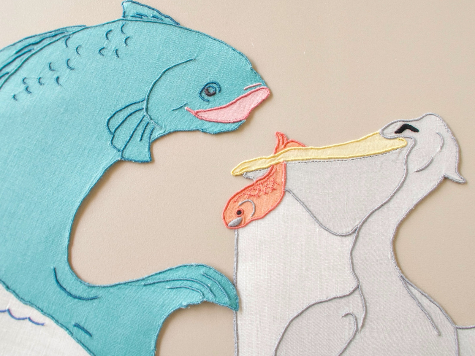 Close-up of vintage Madeira cocktail napkins, teal fish and gray pelican with embroidered fish in bill, hand embroidered linen