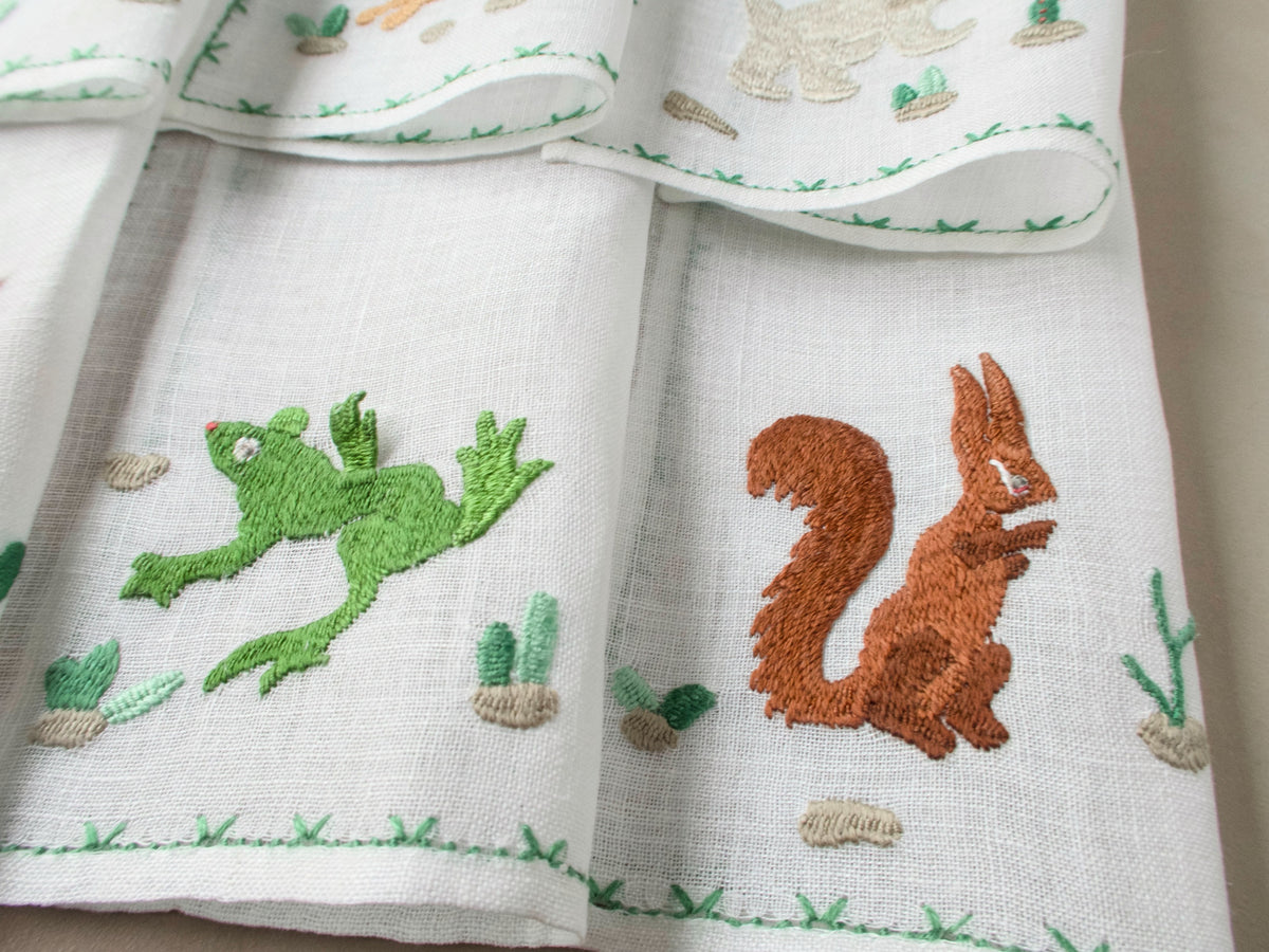 Close-up of Rapisardi squirrel and frog embroidery on white linen cocktail napkins.