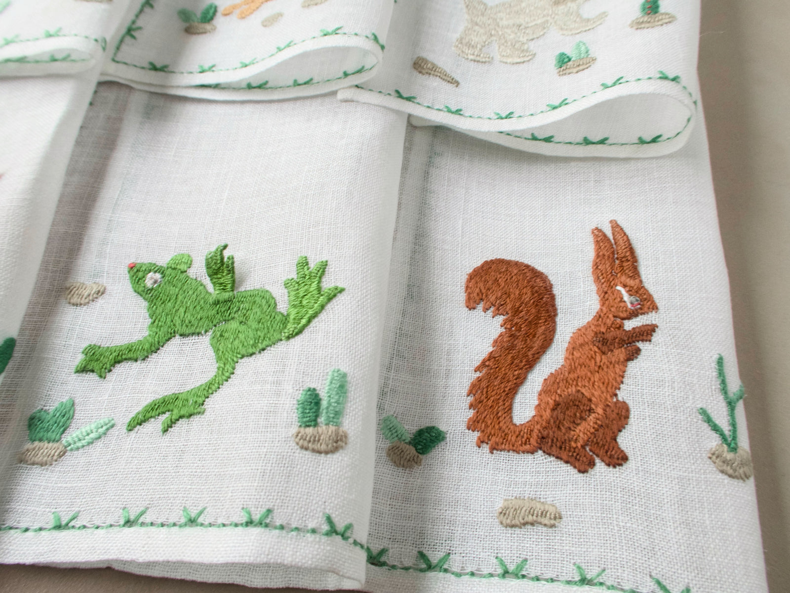 Close-up of Rapisardi squirrel and frog embroidery on white linen cocktail napkins.