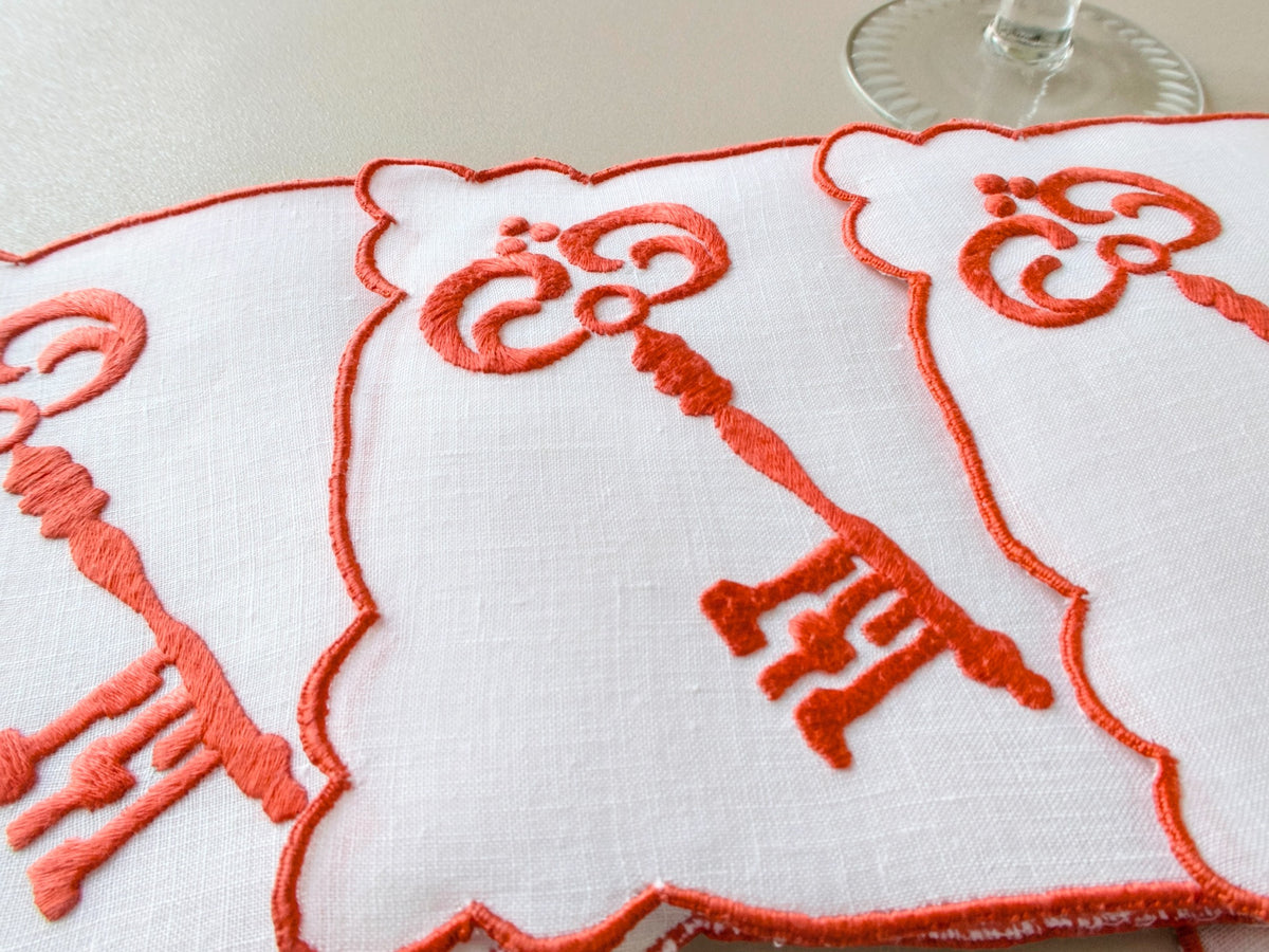 Close-up detail of vintage Madeira hand embroidered skeleton key cocktail napkin, dense red satin stitch on white linen​​​​​​​​​​​​​​​​