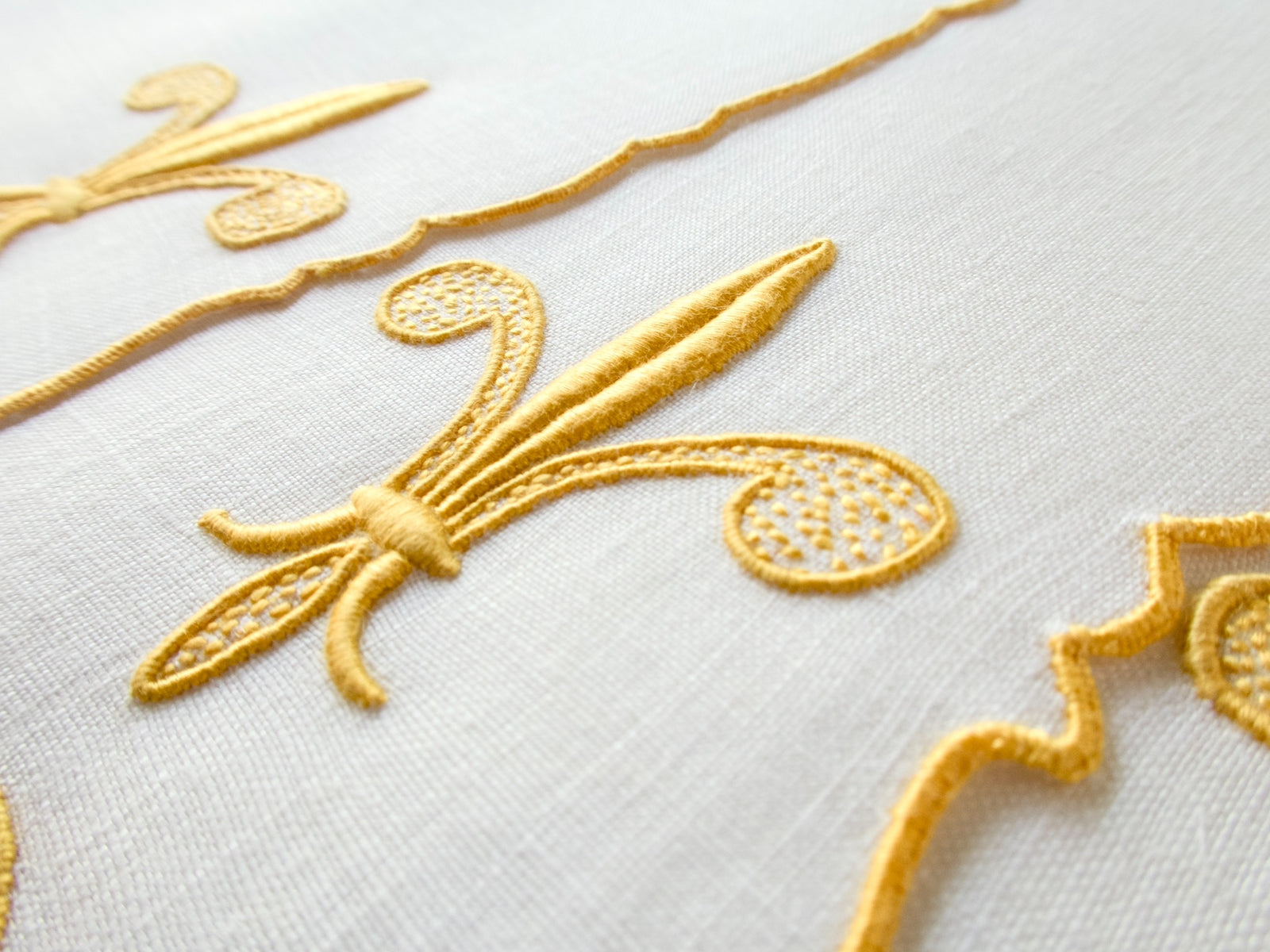 Close-up of vintage Madeira hand embroidered fleur-de-lis, padded satin stitch with openwork fill on white linen