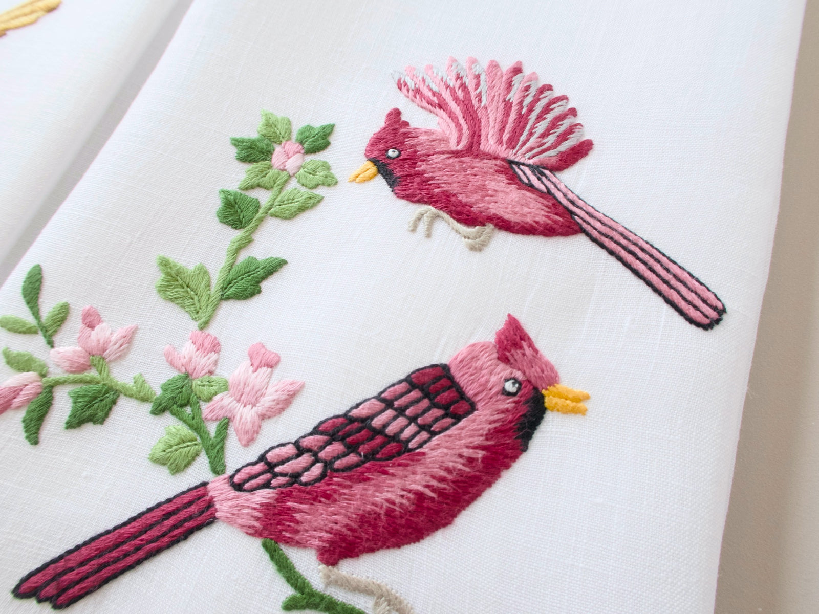 Close-up of vintage Madeira guest towel showing dramatic cardinal embroidery in crimson and magenta with pink blossoms, dimensional satin stitch