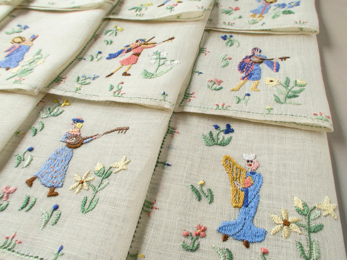 Angled view of several musician napkins layered together, showing different figures and floral borders.