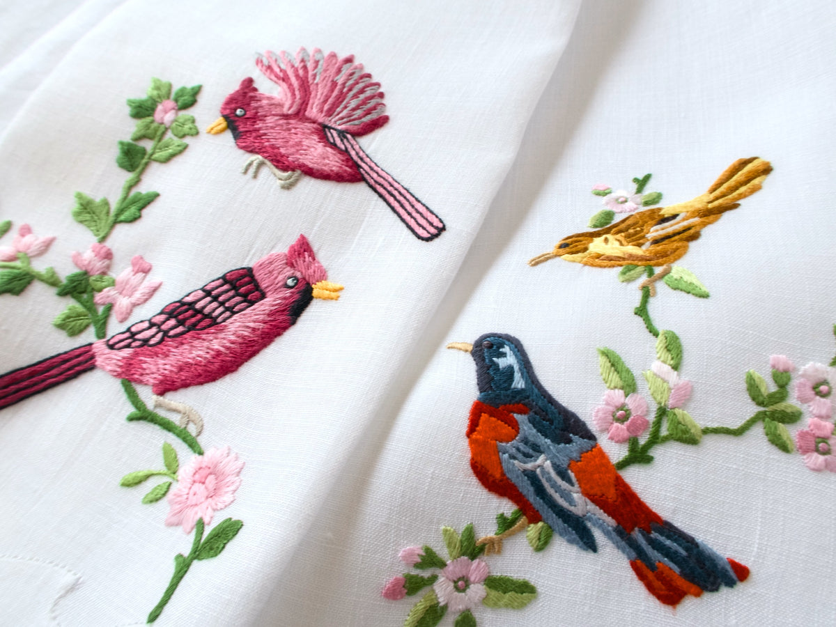 Two vintage Madeira Irish linen guest towels draped together showing coordinating bird embroidery with pink blossoms and green leaves