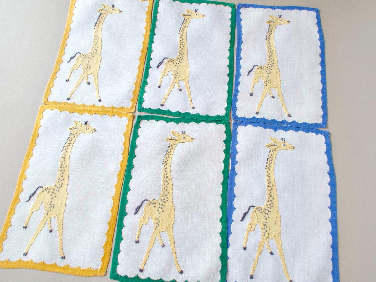 Six vintage Madeira giraffe cocktail napkins arranged in a grid, showing green, yellow and blue border variations