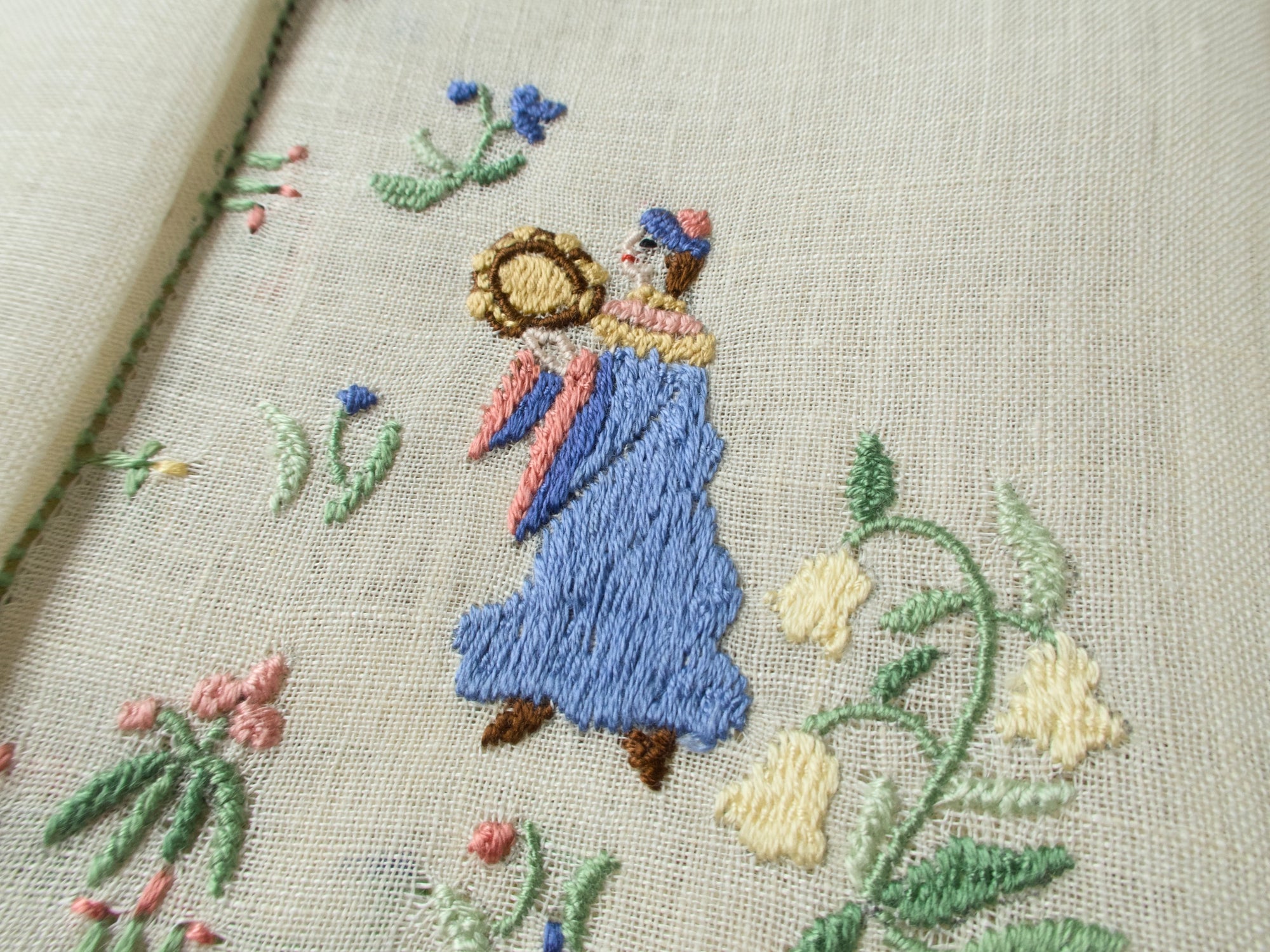Close-up of a dancing musician with a blue dress and tambourine on embroidered linen.