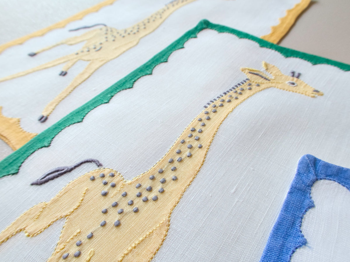 Close-up of vintage Madeira cocktail napkin showing dimensional embroidery and appliqué giraffe detail and colorful repliqué border